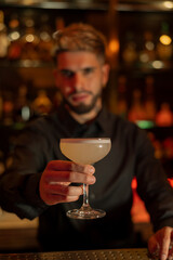 Young elegant barman working behind a bar counter mixing drinks