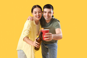 Young couple with beer on yellow background
