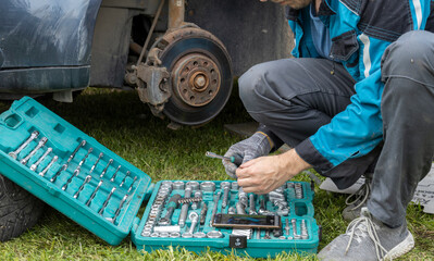 A mechanic is changing a car tire on the roadside, using a socket set and smartphone for guidance,...