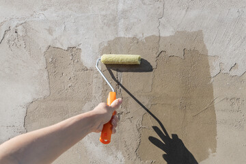 The girl's hand holds a roller dipped in primer and covers the front wall of the house with primer.