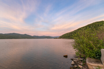 A serene sunset over a tranquil lake with rippled water, mountains in the distance, and a clear sky with soft clouds