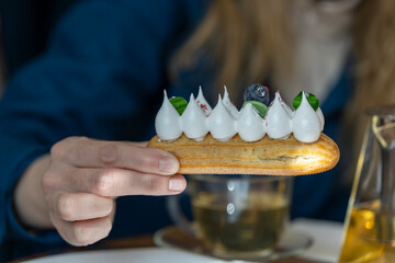 A hand holds a delectable pastry with meringue and cream, garnished with a red dot, on a white...