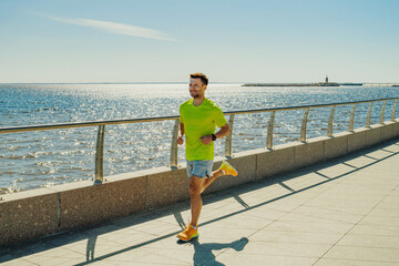 A man in a yellow shirt and shorts jogs along a sunny waterfront promenade, with sparkling water...