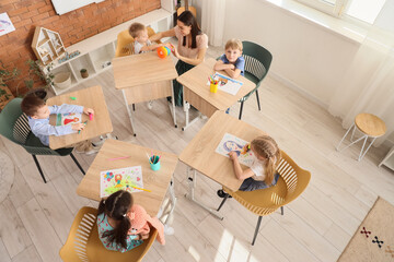 Little children with nursery teacher drawing during art lesson in kindergarten, top view