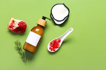 Composition with bottle of cosmetic product, pomegranate and cotton pads on green background