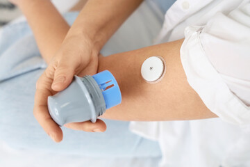 Diabetic woman with glucose sensor measuring blood sugar level in bedroom, closeup