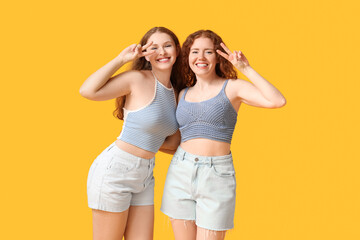 Fototapeta na wymiar Happy redhead sisters showing victory gesture on yellow background