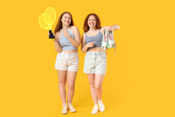 Happy redhead sisters with rollers and badminton rackets on yellow background