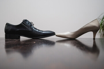 A black men's dress shoe and a beige women's high-heeled pump placed side by side on a reflective...