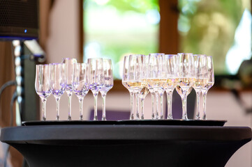 A table with a collection of wine glasses. The glasses are neatly arranged in two rows, with each row containing multiple glasses. The table appears to be placed outdoors, as evidenced by the blurred