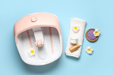 Massage foot bath with spa supplies on color background