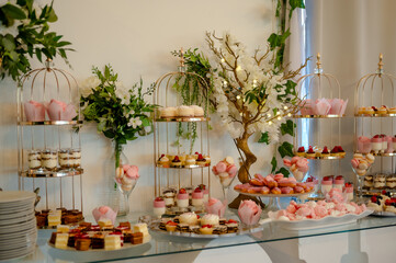 A beautifully arranged dessert table. There are multiple tiered stands, each adorned with a variety of pastries, cakes, and desserts. The stands are decorated with pink ribbons and flowers.
