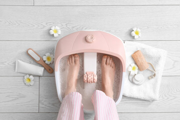 Female legs with massage foot bath and spa supplies on light floor