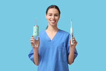 Female dentist with oral irrigator and electric toothbrush on blue background