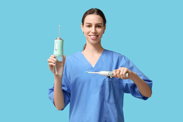 Female dentist with oral irrigator and electric toothbrush on blue background