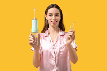 Beautiful young woman with oral irrigator on yellow background