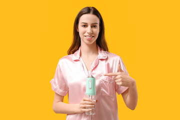 Beautiful young woman pointing at oral irrigator on yellow background