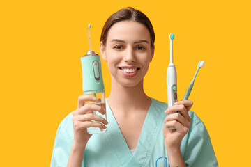 Female dentist with oral irrigator and toothbrushes on yellow background