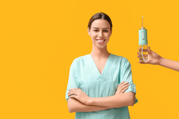 Female dentist and hand with oral irrigator on yellow background