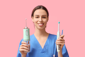 Female dentist with oral irrigator and electric toothbrush on pink background