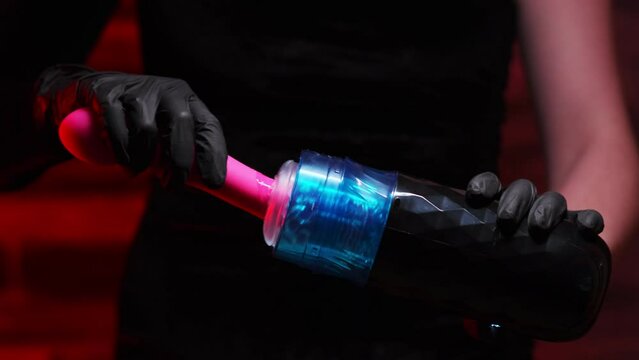 Girl in a black dress and black gloves inserts an artificial pink dildo into an automatic telescopic male masturbator. On a red background. Male massager. Sex shop Adult store, toys for two
