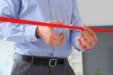 Businessman cutting red ribbon in office, closeup