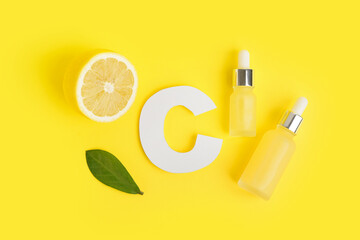Paper letter C, bottles of citrus essential oil and fresh lemon on yellow background