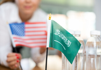 Little flag of Saudi Arabia on table with bottles of water and flag of the USA put next to it by...