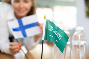 Woman secretary prepares an office for negotiations - she places flags of Saudi Arabia and Finland...