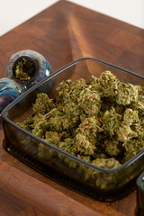 Cannabis bud on a stylish wooden serving tray. Photograph of Marijuana with glass pipe and containers. 