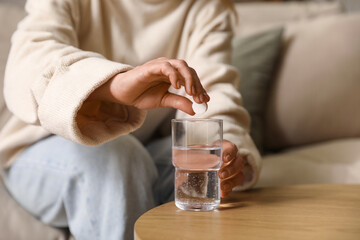 Adult woman suffering from headache with glass of water and soluble tablet at home