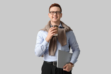 Young man with paper cup of coffee and laptop on grey background