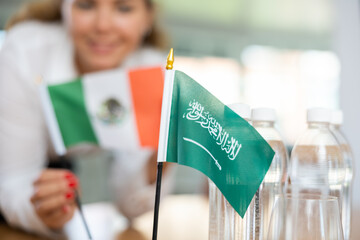 Little flag of Saudi Arabia on table with bottles of water and flag of Mexico put next to it by...