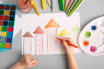 Child's hand drawing houses with markers, paints and pencils on grey background