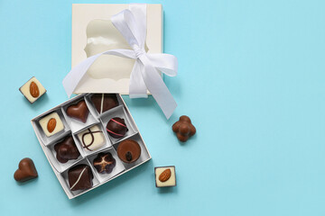 Box with delicious chocolate candies and bow on blue background