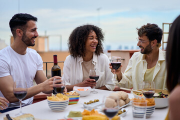 Group of diverse young cheerful friends gathered in a lunch party. Millennial people sitting at a table, with smiles and holding wine glasses enjoying leisure time together