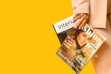 Beautiful young woman with magazines on yellow background, closeup