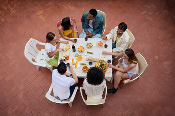 Top view from above of a gathering of people around a table with glasses of wine and food at a happy outdoor celebration terrace party. Young friends enjoying their free time on a summer weekend