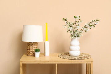 Blooming branches in vase, wicker mat and candle on table near beige wall
