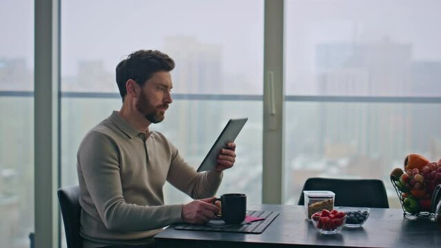 Blurred man reading tablet sitting panoramic kitchen table at morning closeup