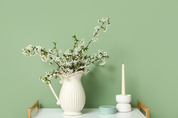 Vase with blooming branches and candle on table near green wall