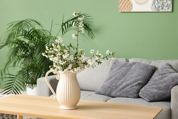 Sofa, houseplant and vase with beautiful blooming branches on table in interior of stylish living room