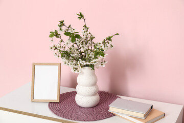 Empty photo frame and vase with beautiful blooming branches on chest of drawers near pink wall
