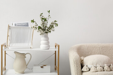 Blooming branches in vase and holder with magazines on shelving unit near white wall