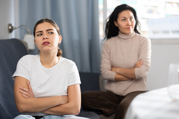 European woman sitting at table at home while having quarrel with her friend in apartment.