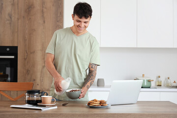 Young man pouring milk into bowl with corn balls in kitchen