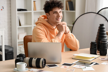 Professional happy male photographer with modern camera and laptop sitting in studio