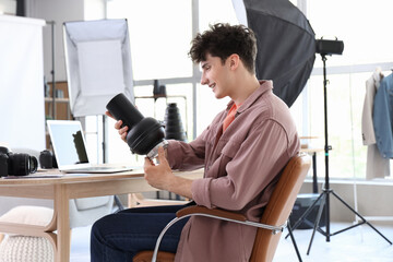 Professional happy male photographer with lens of modern camera sitting on chair in studio