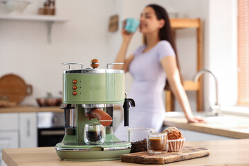 Beautiful young woman with cups of coffee and modern machine in kitchen
