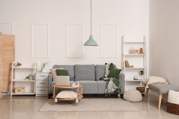 Modern interior of living room with grey sofa and laptop on table